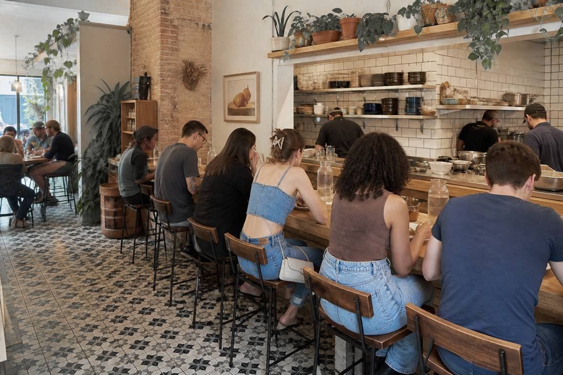 Diners at a busy restaurant counter with an open kitchen